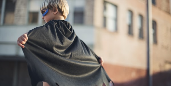 selective focus photography of boy wearing black Batman cape