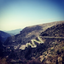 A winding mountain road cutting through rugged terrain with a clear blue sky overhead.