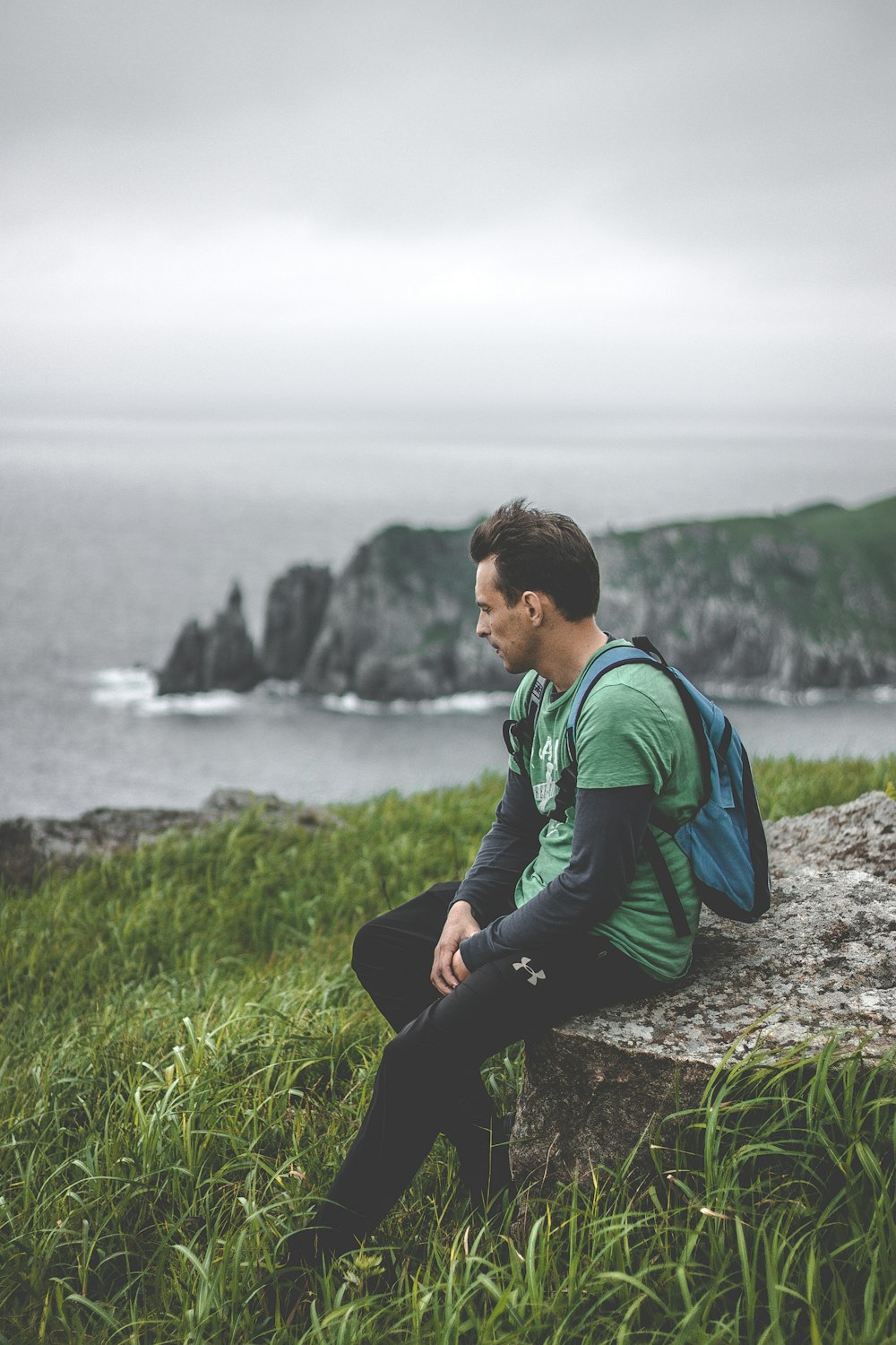 man sitting on gray rock with green grass