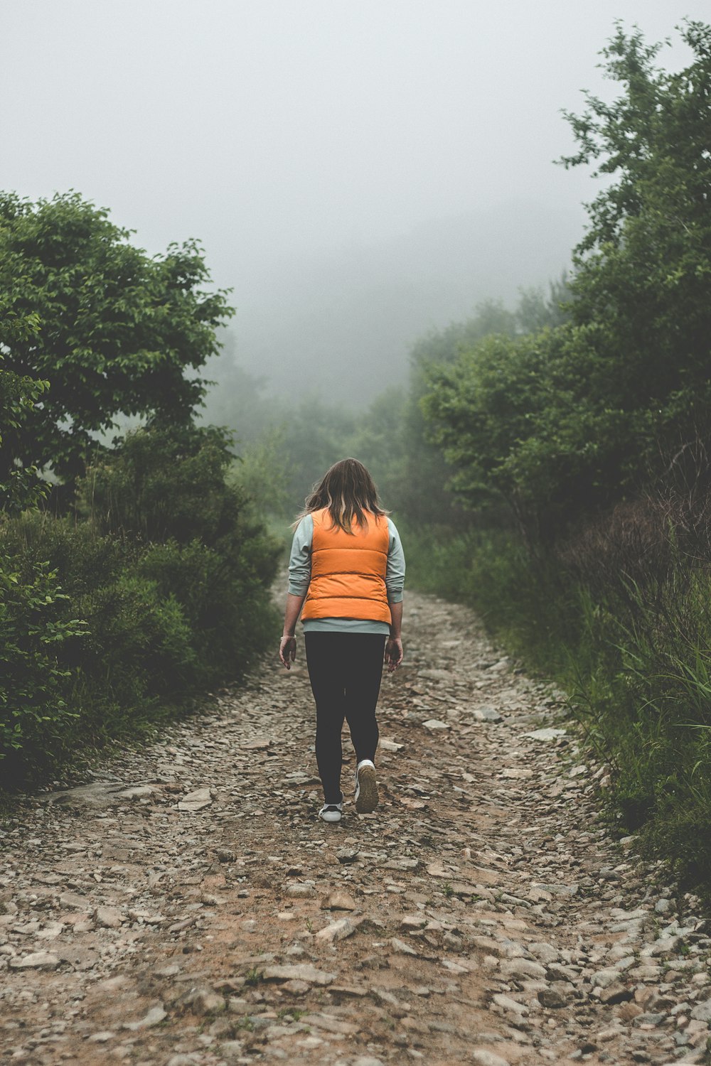 woman wearing orange life vest walking on pathway during daytime
