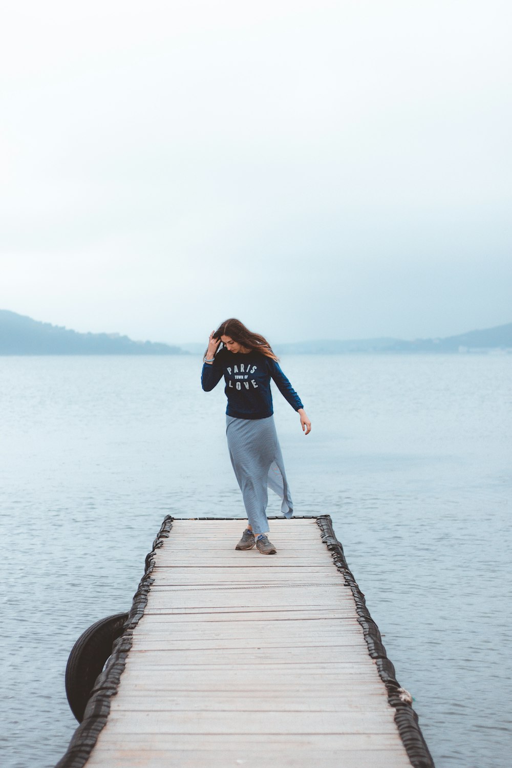 woman standing in the middle of wooden footbridge leading to the sea