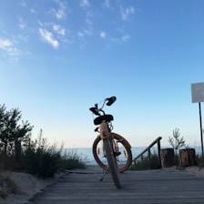 Bicyclists pausing on a coastal trail with clear blue sea and golden beach in view.