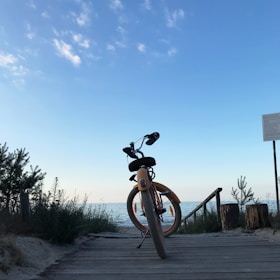Bicyclists pausing on a coastal trail with clear blue sea and golden beach in view.
