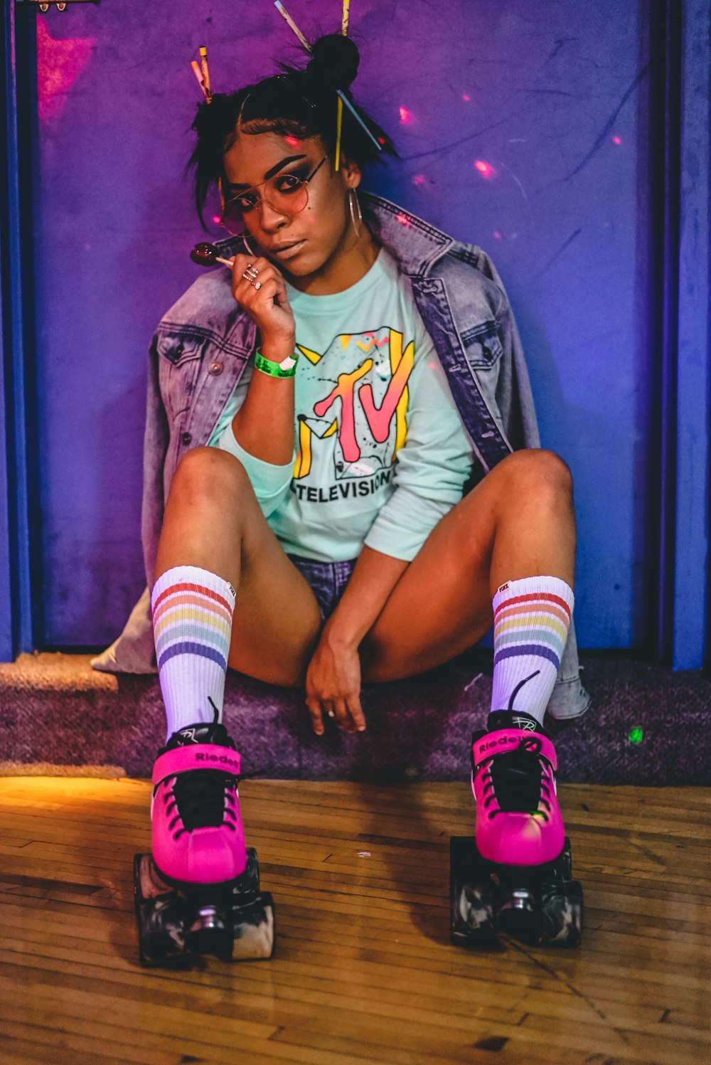 woman sitting wearing roller skates and jacket while holding lollipop