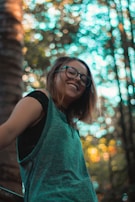 Smiling person outdoors wearing blue light glasses with sunlight filtering through trees