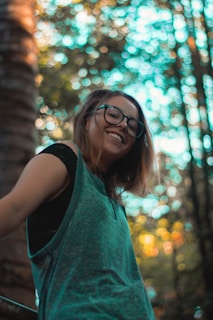 Smiling person outdoors wearing blue light glasses with sunlight filtering through trees