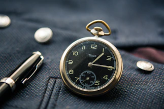 A close-up of a classic wristwatch resting on a wooden desk beside a vintage fountain pen.