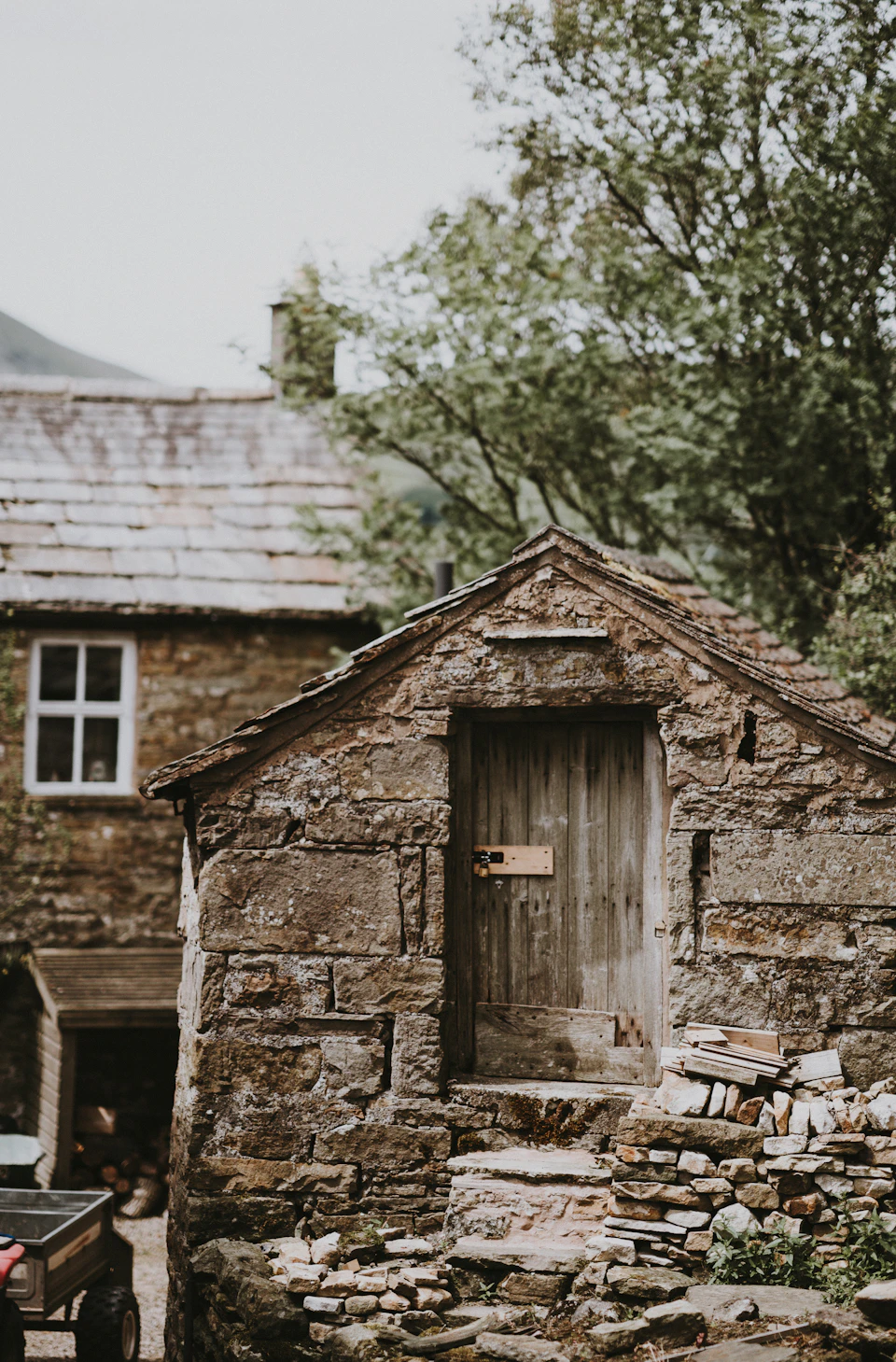 Quaint stone building with wooden door and window on dirt path surrounded by lush greenery