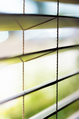 Horizontal window blinds partially open, allowing soft natural light to filter through, creating an interplay of light and shadow. The background is blurred, giving a serene and peaceful atmosphere.