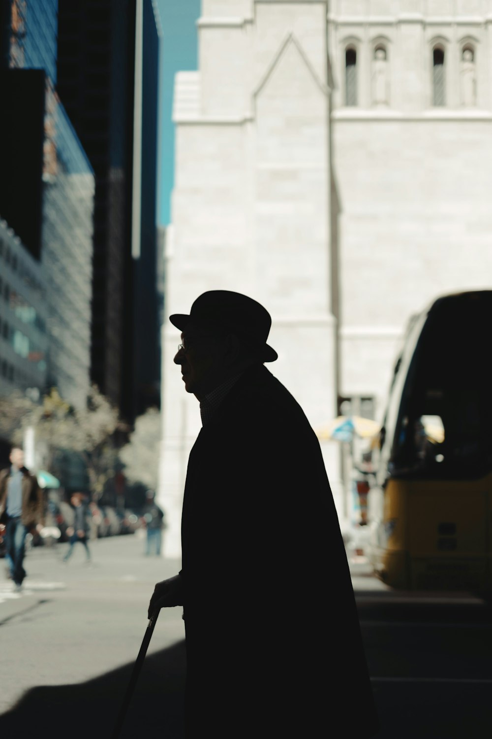 silhouette di uomo che tiene bastone da passeggio sulla strada durante il giorno