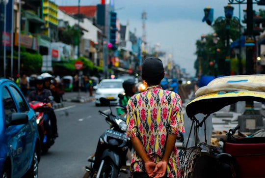 man standing near black motorcycle with passing vehicles during daytime in Yogyakarta City Indonesia