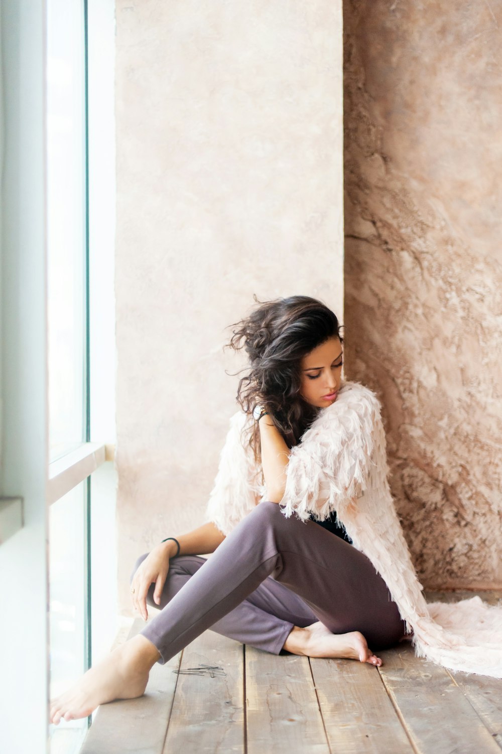 woman sitting beside white wall in front glass window