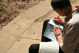A person journaling outdoors, surrounded by nature and sunlight.