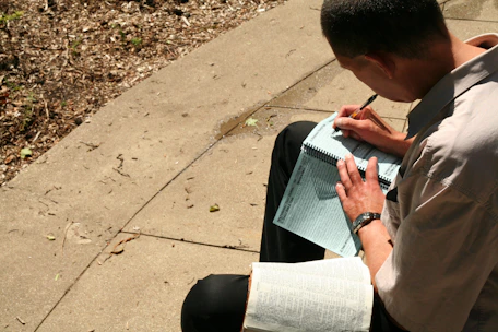 A person journaling outdoors surrounded by nature and sunlight.