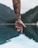 A tattooed arm extends over a body of water, with a wristband featuring a motivational phrase. The serene background includes blurred mountains and a reflective lake.