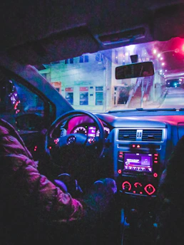 A sleek car dashboard glowing with neon purple and green lights at night.