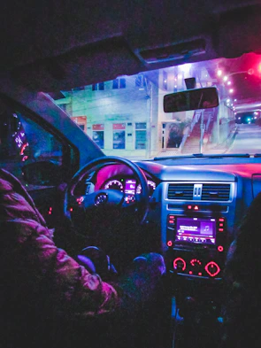 Nighttime city street with a high-performance car’s illuminated dashboard glowing neon red.