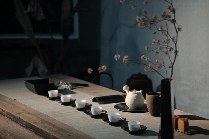 A tea set of small white cups and a teapot on a low wooden table