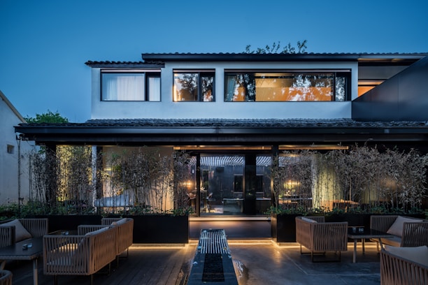 A modern two-story house with large windows and a well-kept garden under a clear blue sky.