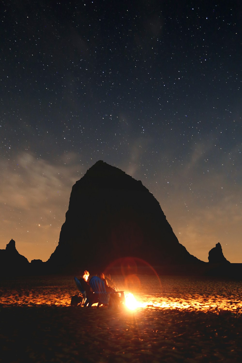 photo of couple sitting in front of bonfire near mountain
