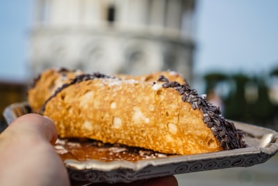 Artisan hands delicately filling a cannolo with fresh ricotta cream beside golden Sicilian fresco patterns.