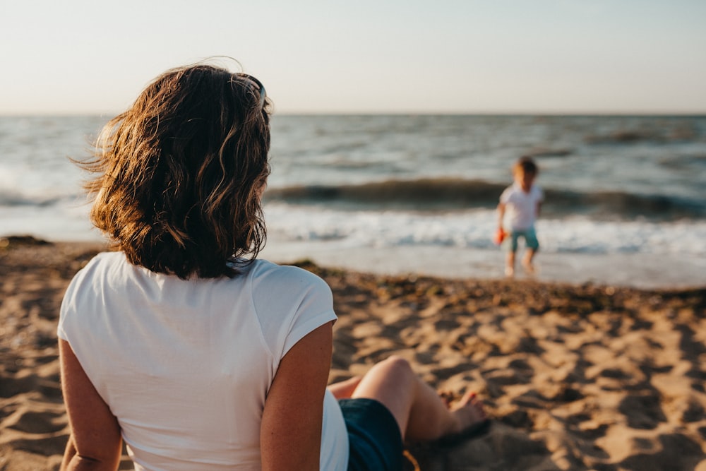 Mujer que observa al niño que juega en la playa durante el día