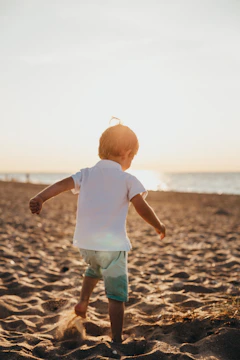 Children playing barefoot on soft sand with warm sunlight filtering through nearby trees.