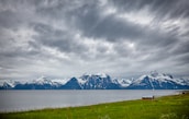 body of water next to snow capped mountain under gray cloudy sky