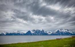 body of water next to snow capped mountain under gray cloudy sky