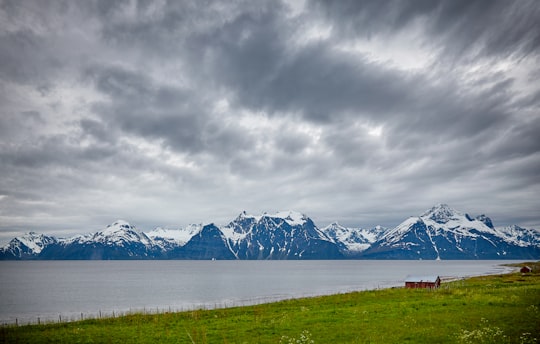 body of water next to snow capped mountain under gray cloudy sky in Lyngen Alps Norway