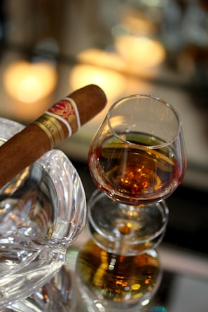 A warm, inviting scene with a lit cigar and a glass of whiskey on a rustic surface.
