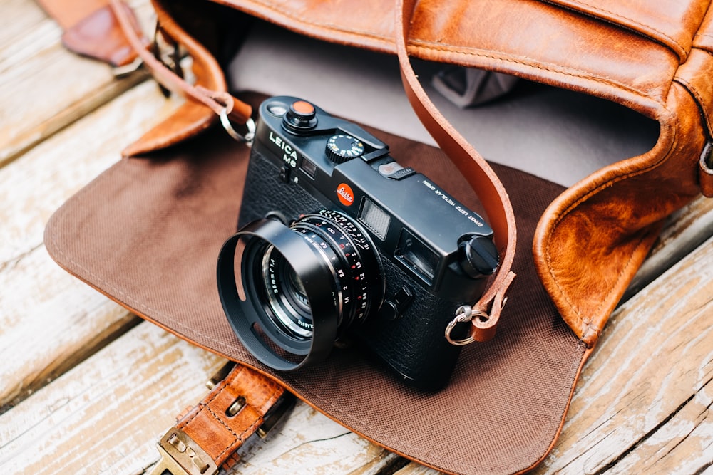 black DSLR camera with brown leather bag on brown surface