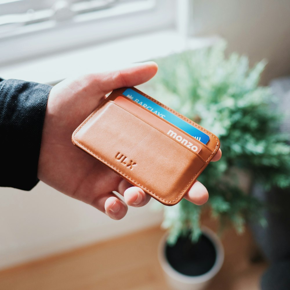 person holding brown ULX leather wallet