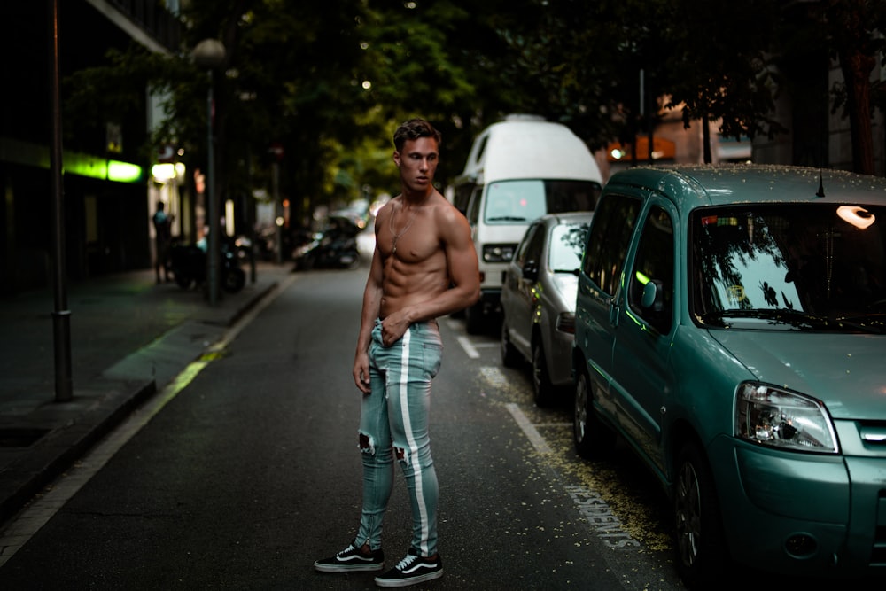 man wearing blue Amiri denim track pants standing beside green car