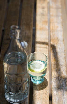 A serene morning scene with a glass of water and fresh lemon on a wooden table by a sunlit window.