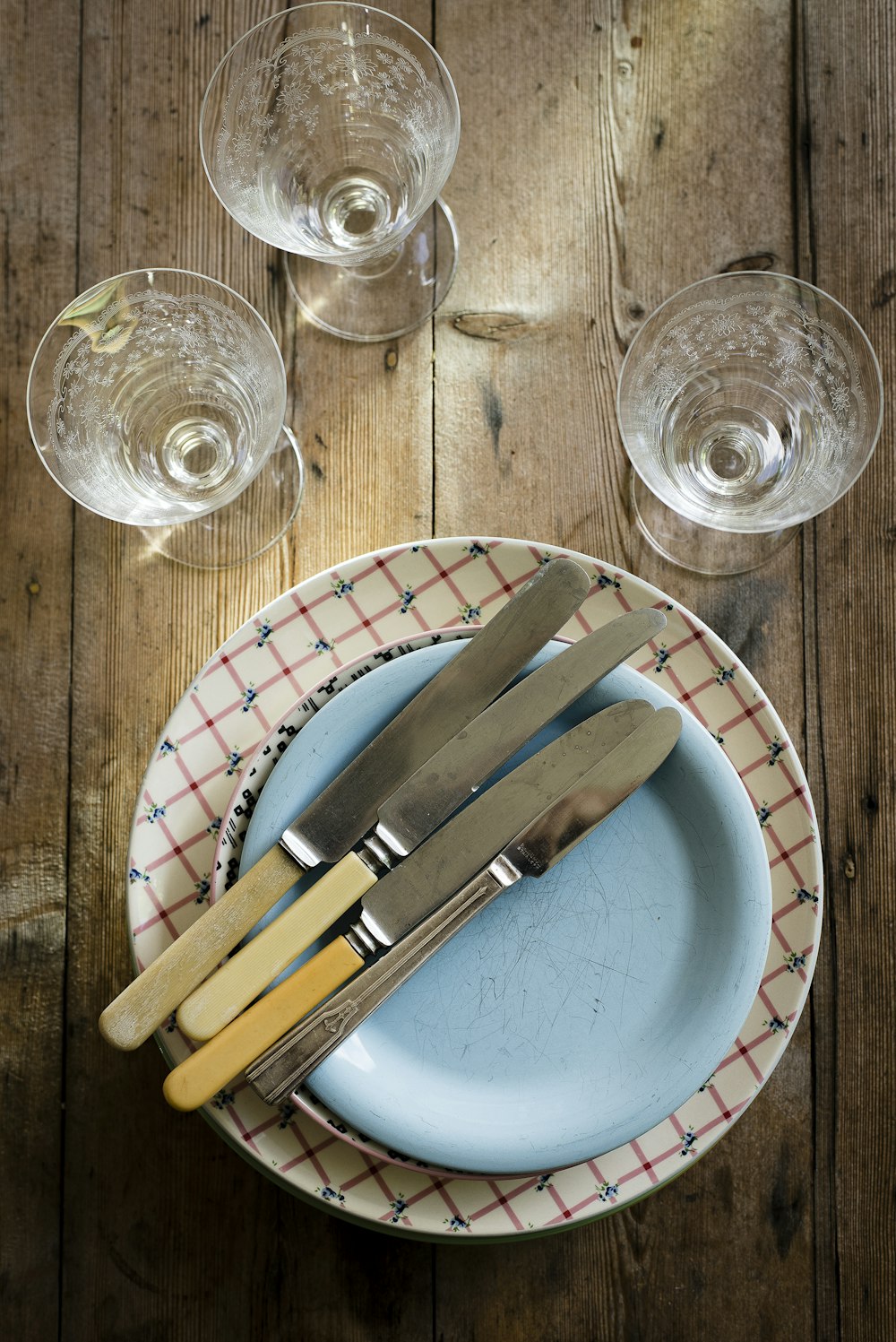 fotografia plana de copos de caule, pires, prato e facas de pão e manteiga