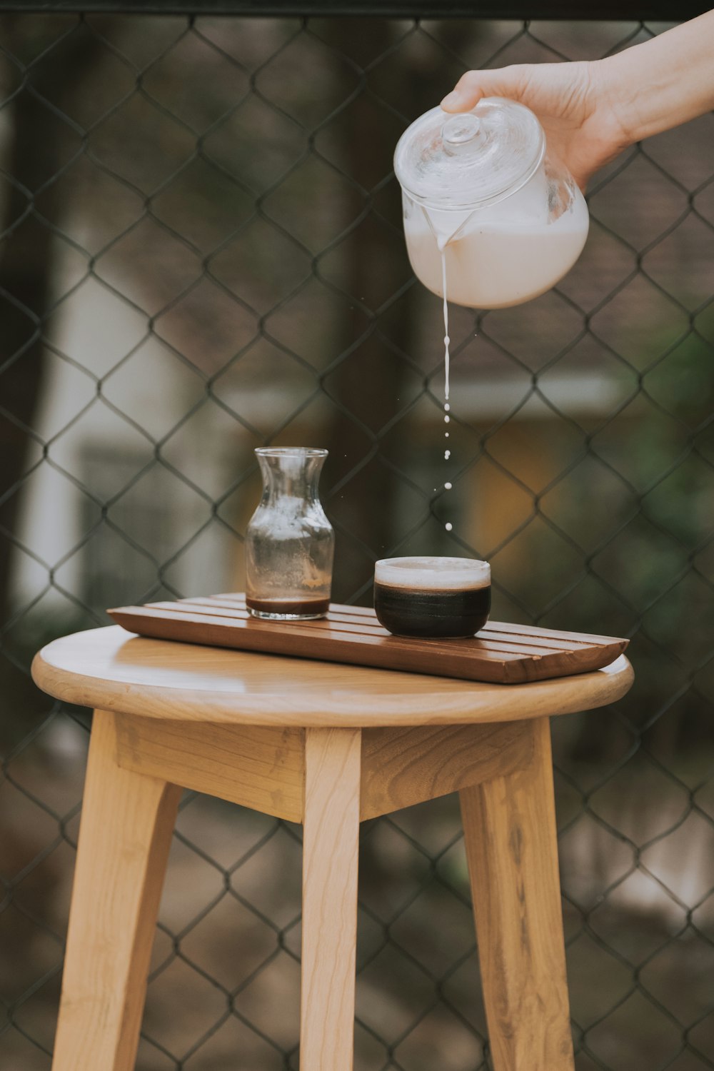 person holding clear glass pitcher pouring round black cup