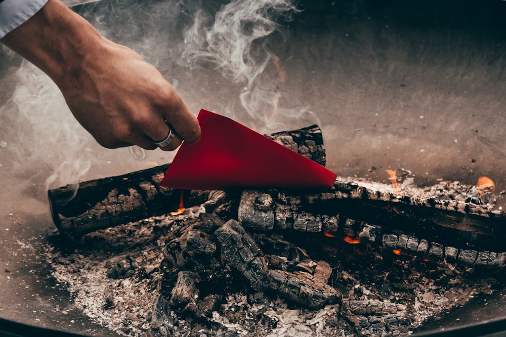 person holding red paper near charred wood