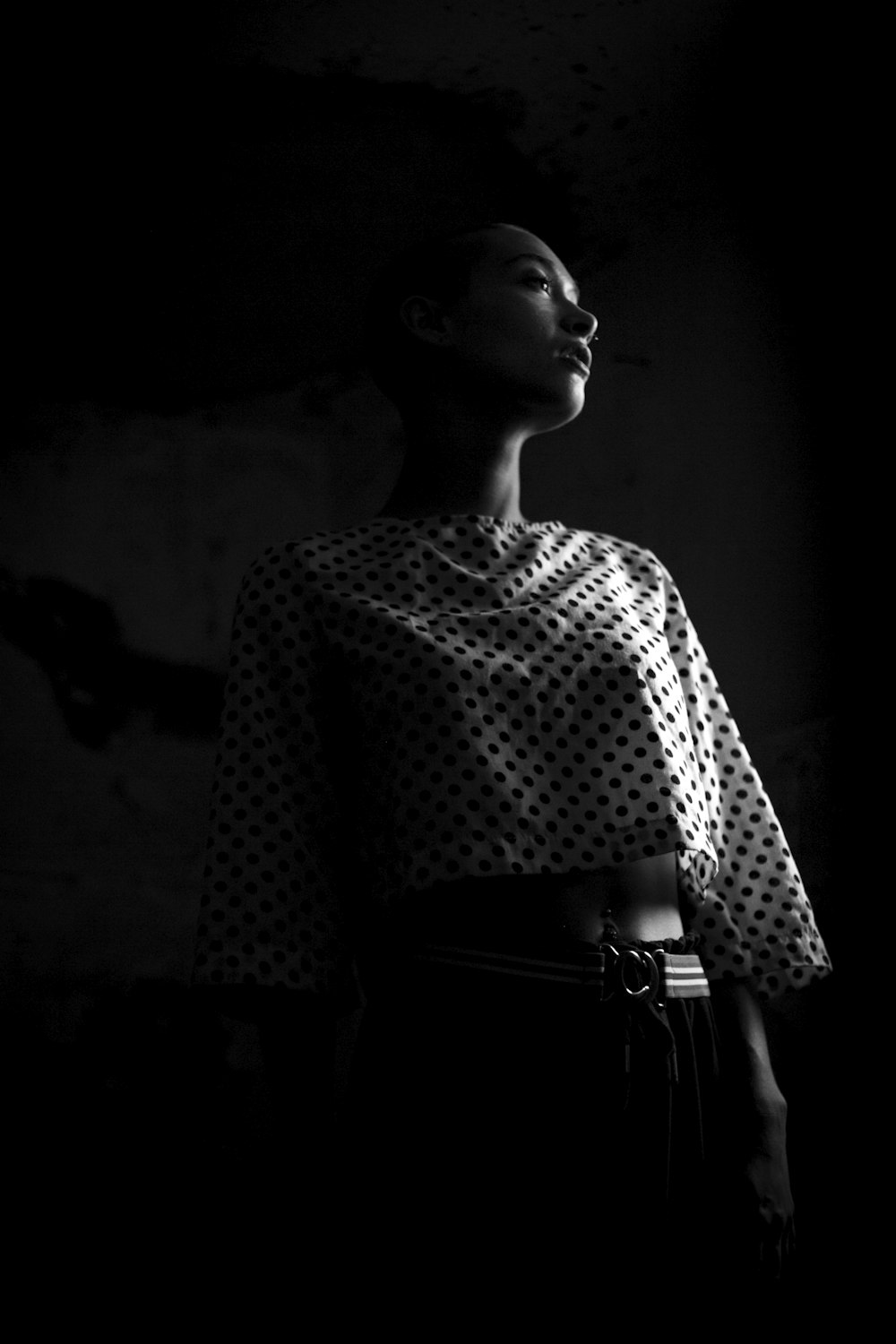 어두운 방에 서 있는 흑백 물방울 무늬 크롭을 입은 여자의 로우 앵글 사진