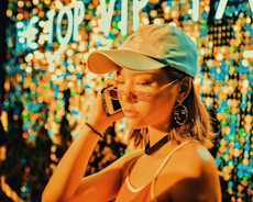 woman wearing tank top, fitted cap and sunglasses holding a phone on right ear