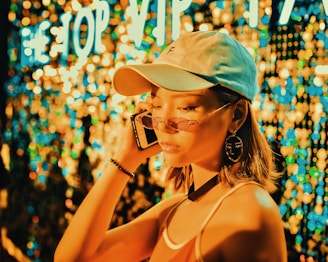 woman wearing tank top, fitted cap and sunglasses holding a phone on right ear