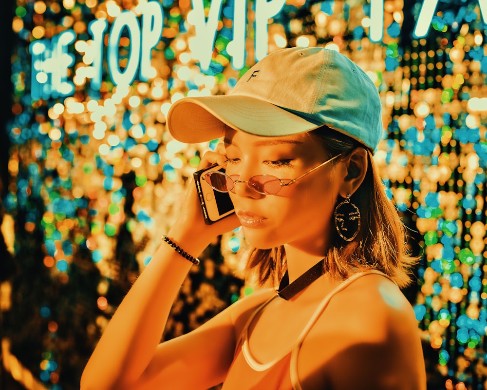 woman wearing tank top, fitted cap and sunglasses holding a phone on right ear