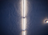 A fluorescent light tube is mounted on a textured ceiling, providing a bright, even glow. The light creates a shadowy effect along the sides, with additional small light reflections visible to the right.