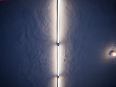 A fluorescent light tube is mounted on a textured ceiling, providing a bright, even glow. The light creates a shadowy effect along the sides, with additional small light reflections visible to the right.