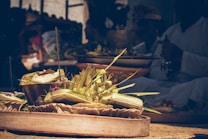 A close-up view of traditional offerings made with woven palm leaves and flowers, arranged in decorative baskets. The ambient lighting creates a warm, serene atmosphere, enhancing the intricate details of the offerings.