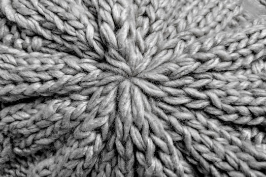 A close-up view of a knitted fabric displaying a textured pattern of interwoven yarns. The fibers are thick, creating a pronounced and intricate design with a star-shaped center.