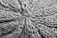 A close-up view of a knitted fabric displaying a textured pattern of interwoven yarns. The fibers are thick, creating a pronounced and intricate design with a star-shaped center.