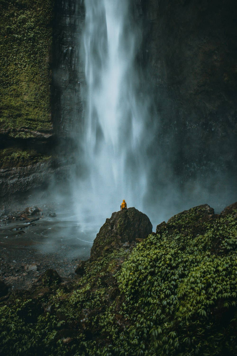 person sitting on rock in front of waterfalls