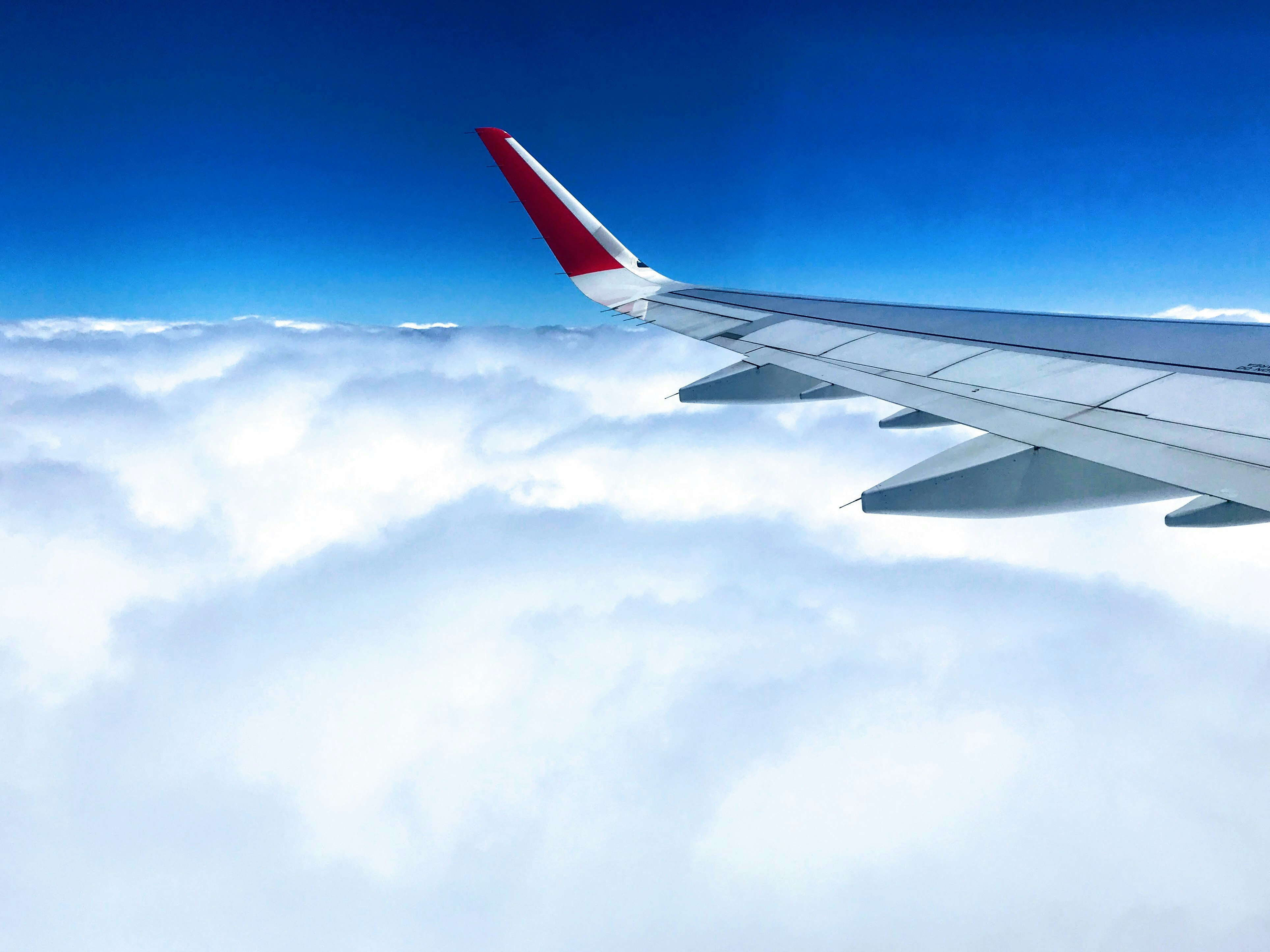 white and red airplane wing above cloudy skies