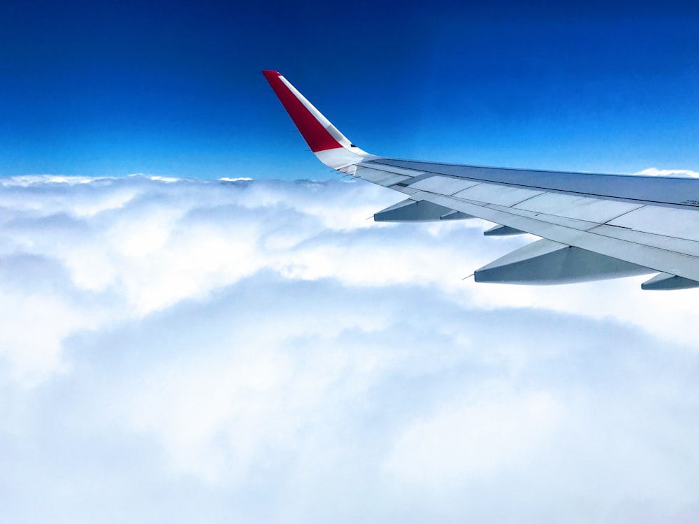 white and red airplane wing above cloudy skies